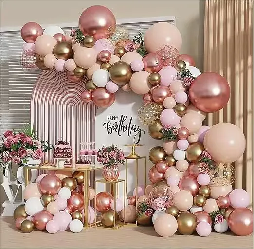 A rose gold and blush balloon garland arching over a styled dessert table