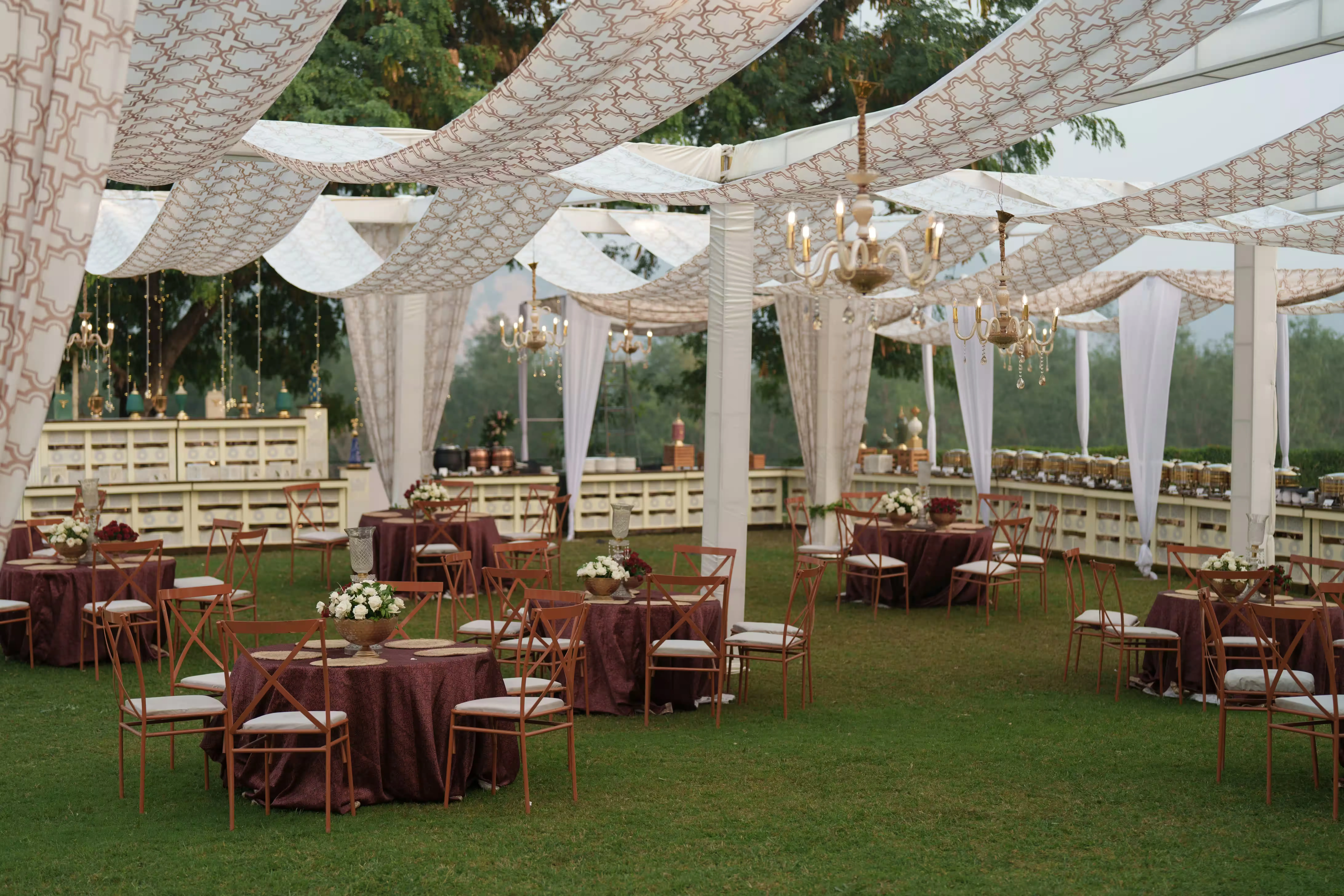 A draped outdoor tent styled with fairy lights, linen canopies and candlelit tables for an evening celebration