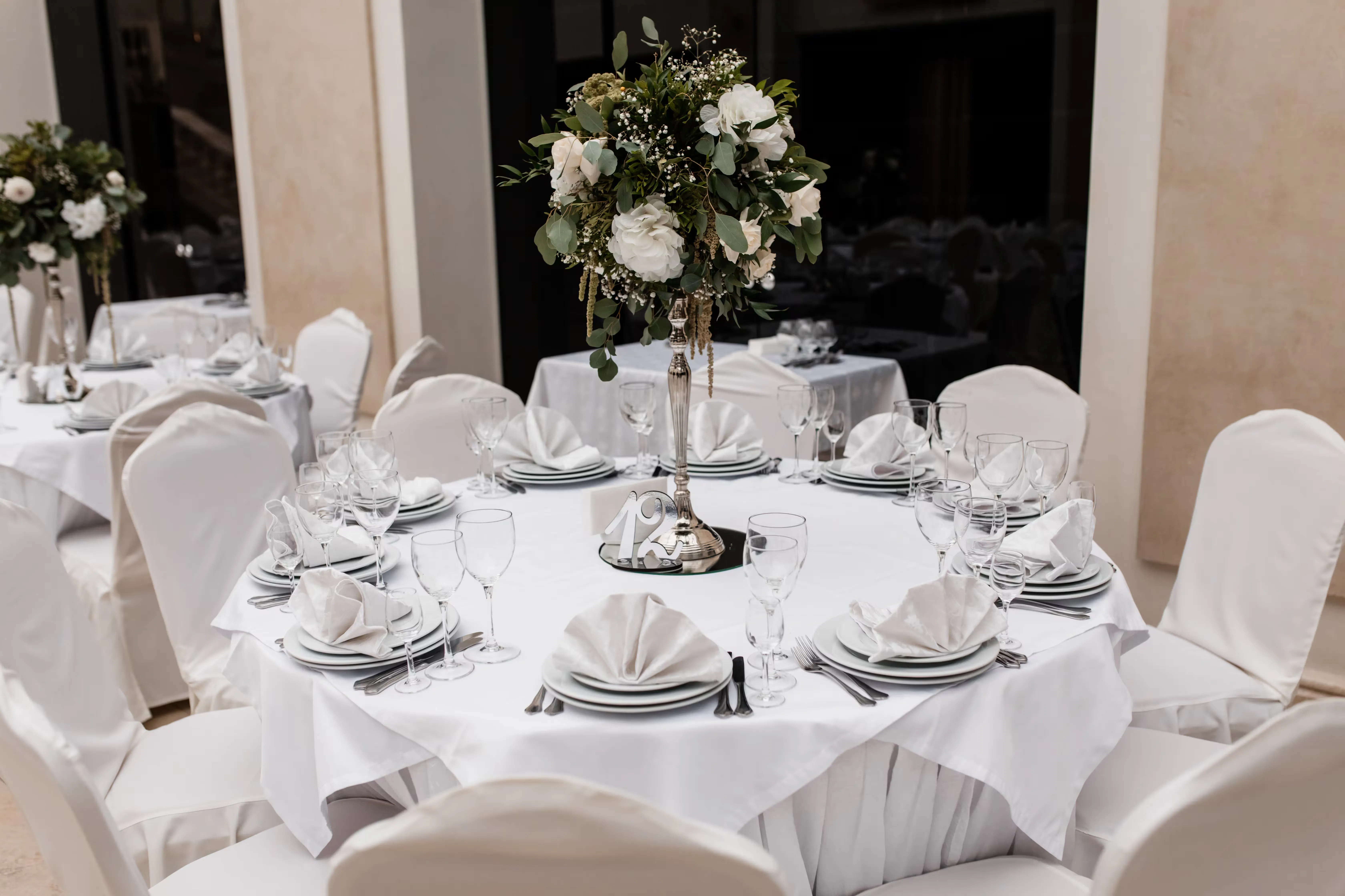 A round table set with white linen, tall floral centrepiece and full glassware